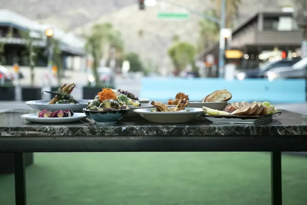 Food spread on an outdoor table, blurred city and mountains.