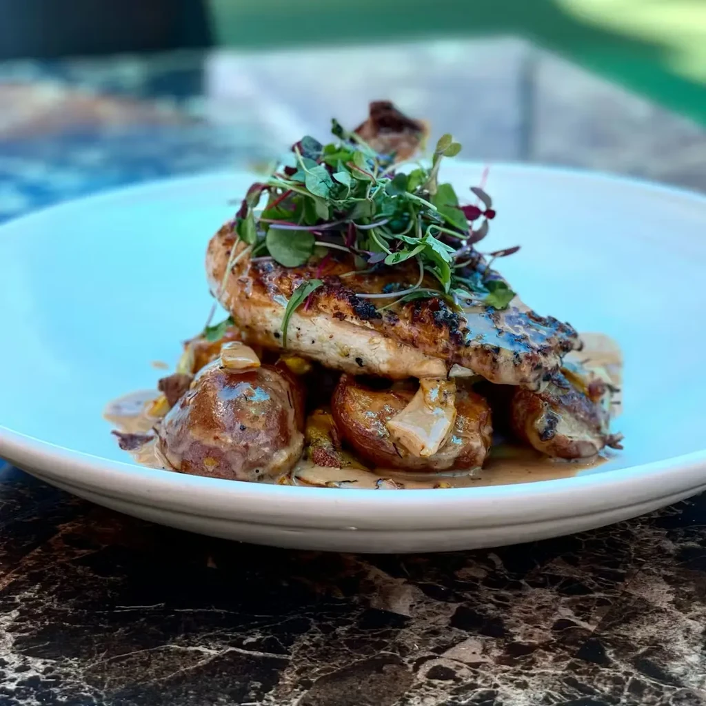 Grilled chicken, microgreens, roasted potatoes, and creamy mushroom sauce on a plate.