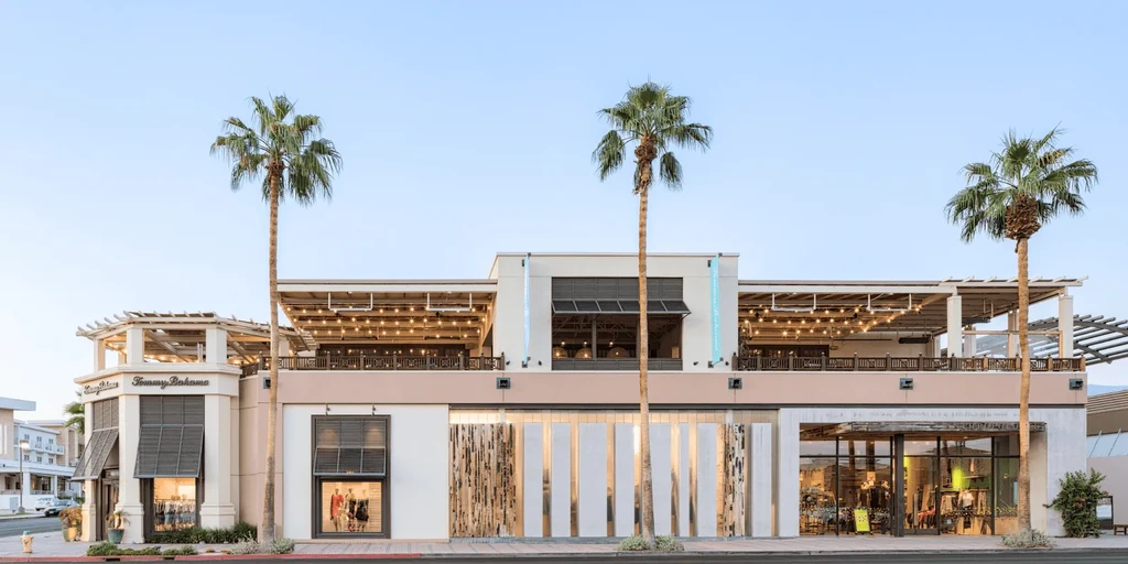 Modern multi-story Tommy Bahama building with palm trees and a lit patio.