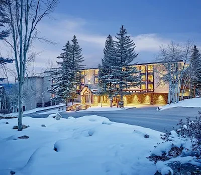 Warmly lit lodge at dusk in a snowy winter landscape.