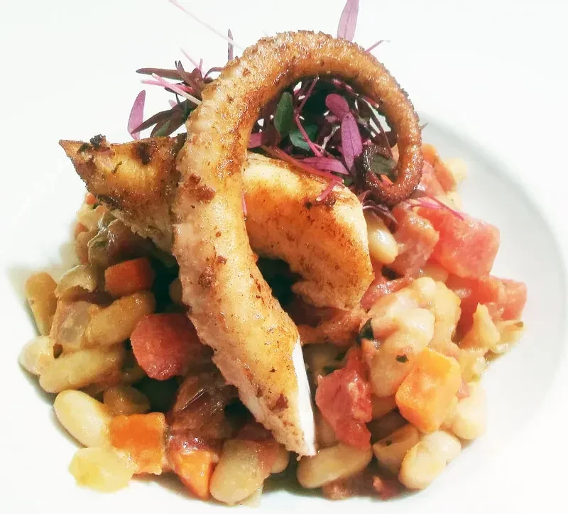 Grilled octopus tentacles on white bean salad, garnished with microgreens.