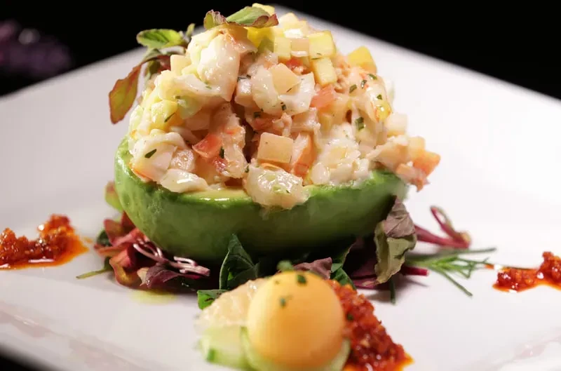 Avocado half with seafood salad, mixed greens, and relish on plate.