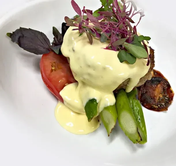 Meticulously plated Eggs Benedict variation with asparagus, tomatoes, and herbs.