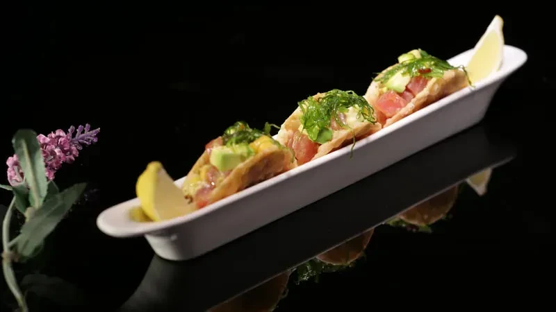 Three poke tacos with fish, avocado, and seaweed on a white plate.