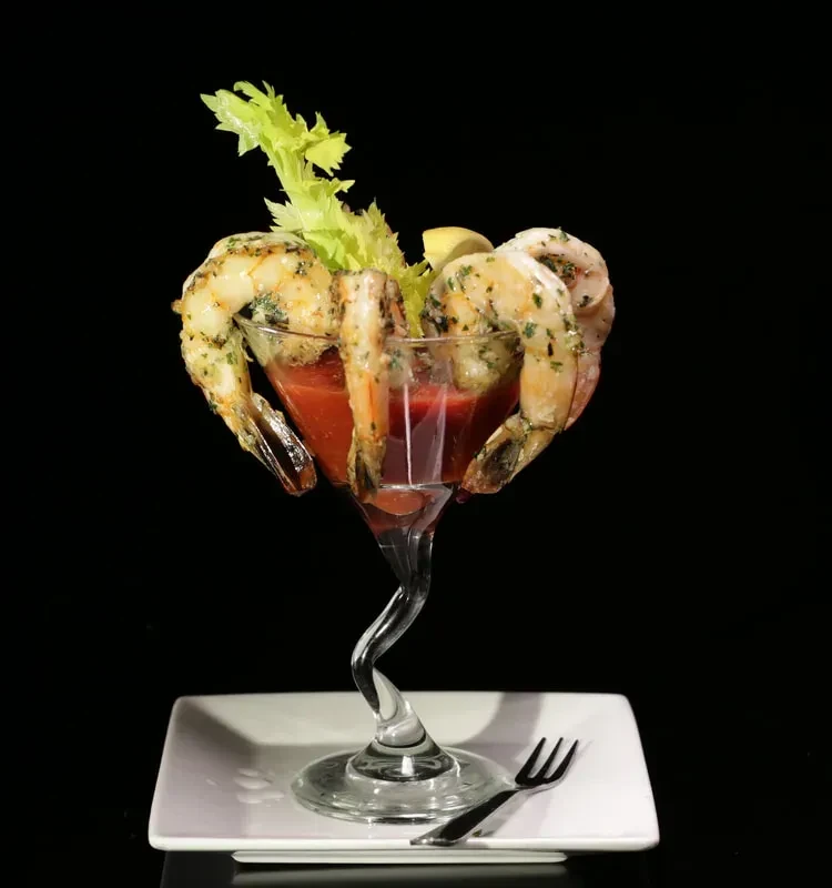 Gourmet shrimp cocktail in a twisted-stem glass with celery and lemon.