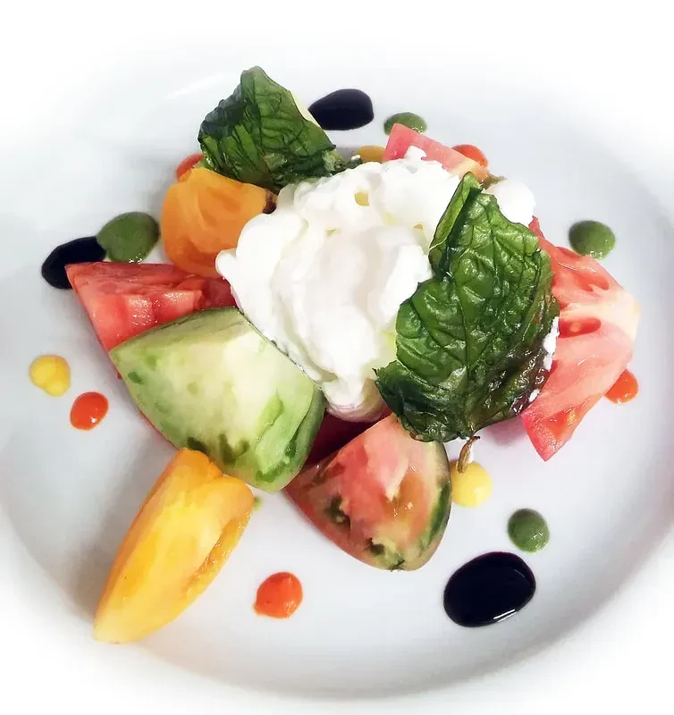 Gourmet salad with burrata, heirloom tomatoes, basil, and colorful sauces.