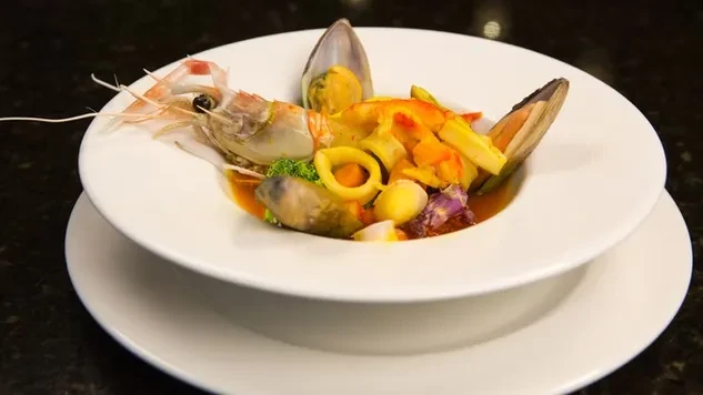 Gourmet seafood dish with prawn, mussels, vegetables, in orange broth.