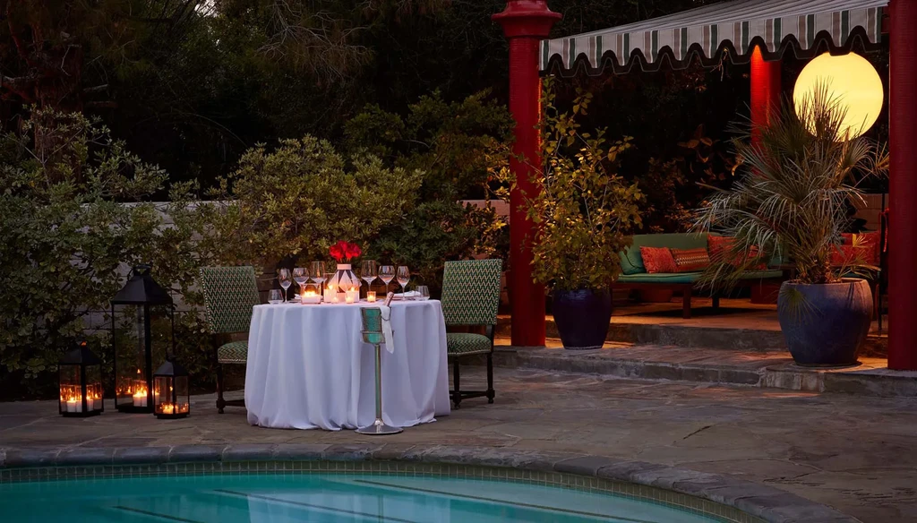 Luxurious outdoor dining table set for two by a pool at dusk.
