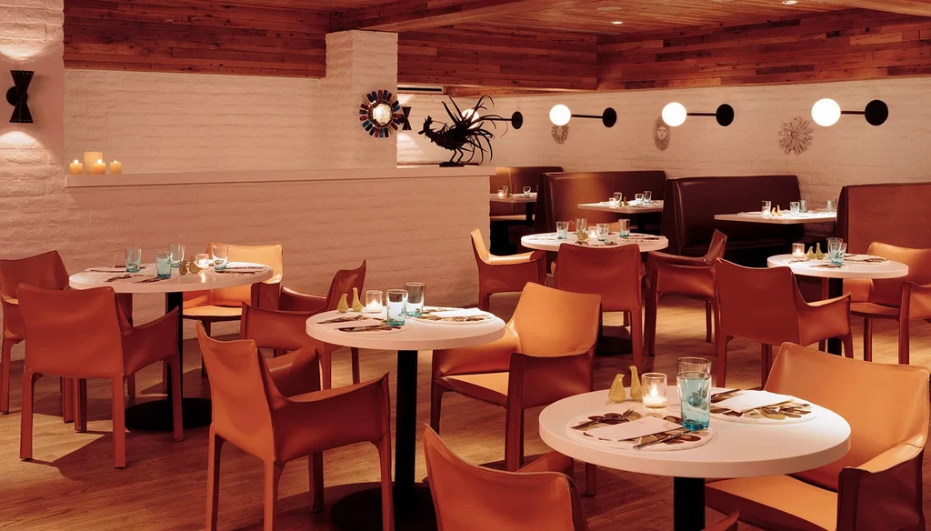 Empty restaurant dining area with warm colors, wooden ceiling, and set tables.