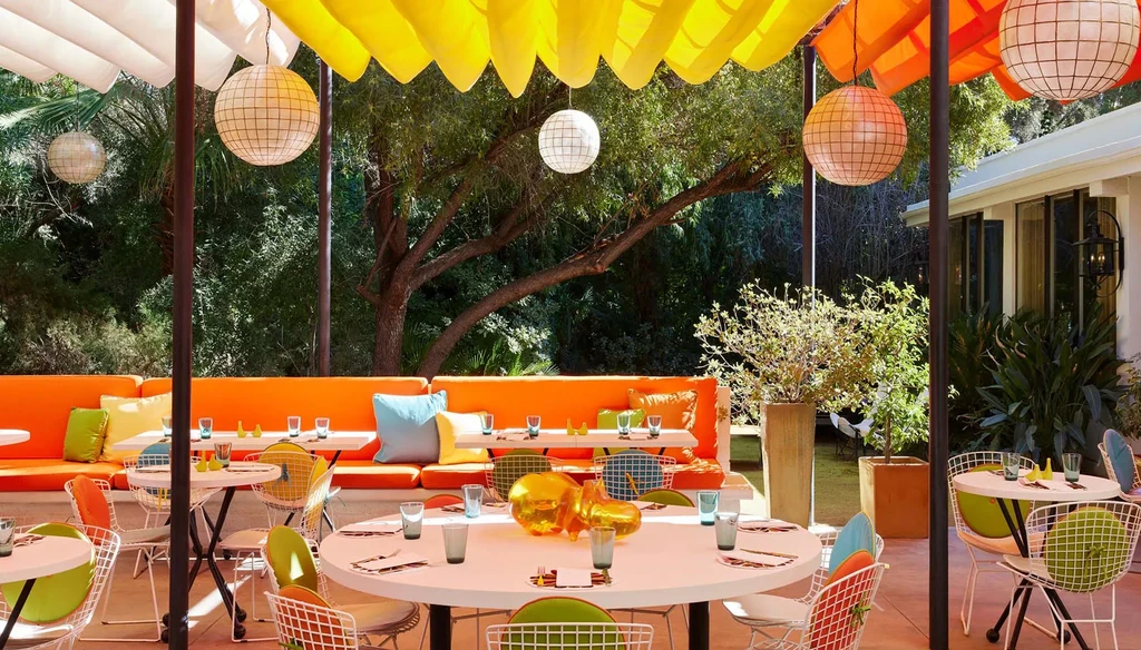 Colorful outdoor restaurant patio with set tables, bright seating, and awnings.
