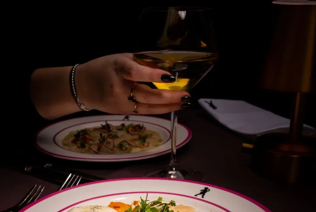 Close-up of hand holding wine, two gourmet appetizers on dark table.