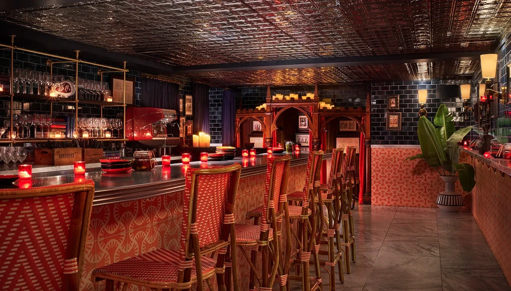 Warmly lit upscale bar with rattan stools, pressed-tin ceiling, and tiled walls.
