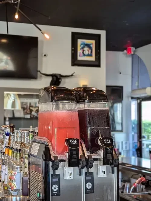 Dual frozen drink machine with colorful beverages in a modern bar.