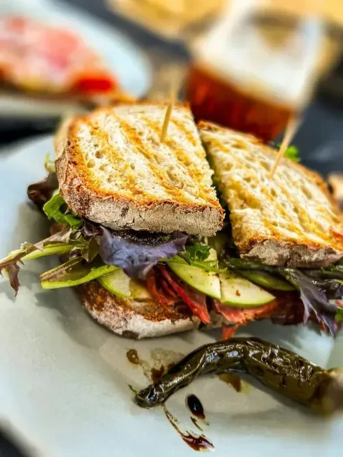 Diagonal-cut gourmet sandwich with deli meat, greens, and glazed pepper.