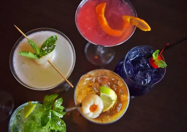 Five distinct, colorful cocktails with unique garnishes on a dark surface.