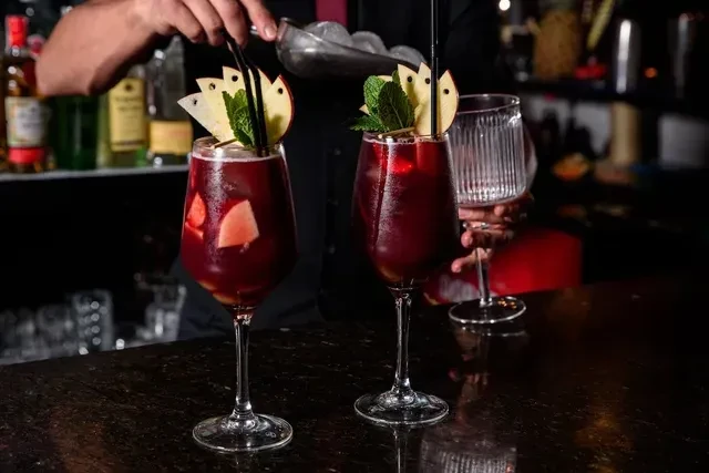 Close-up of two garnished red cocktails with a bartender adding ice.