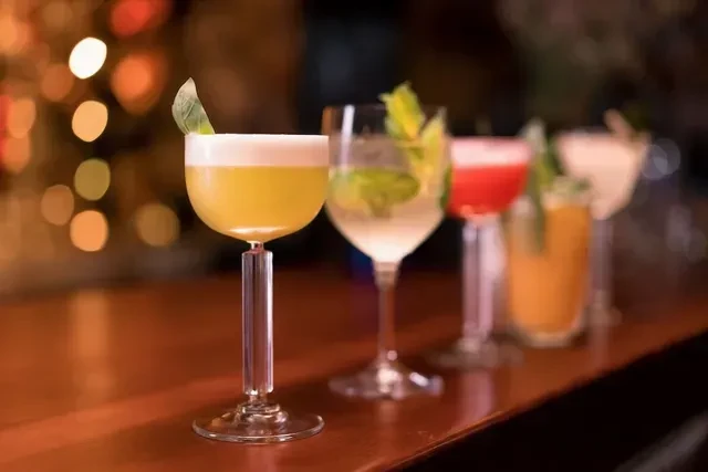 Five cocktails on a wooden bar, yellow one with foam in focus.