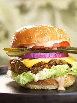 Plant-based burger with sesame bun, tomato, purple onion, cheese, and pickle.