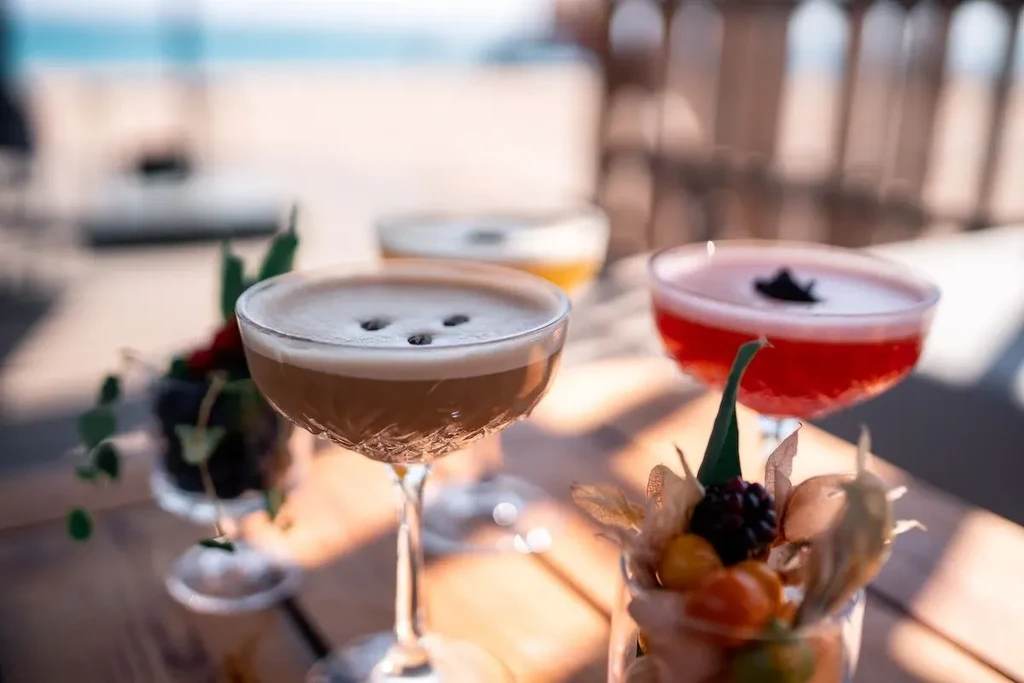 Close-up of three garnished cocktails on a rustic wooden table outdoors.