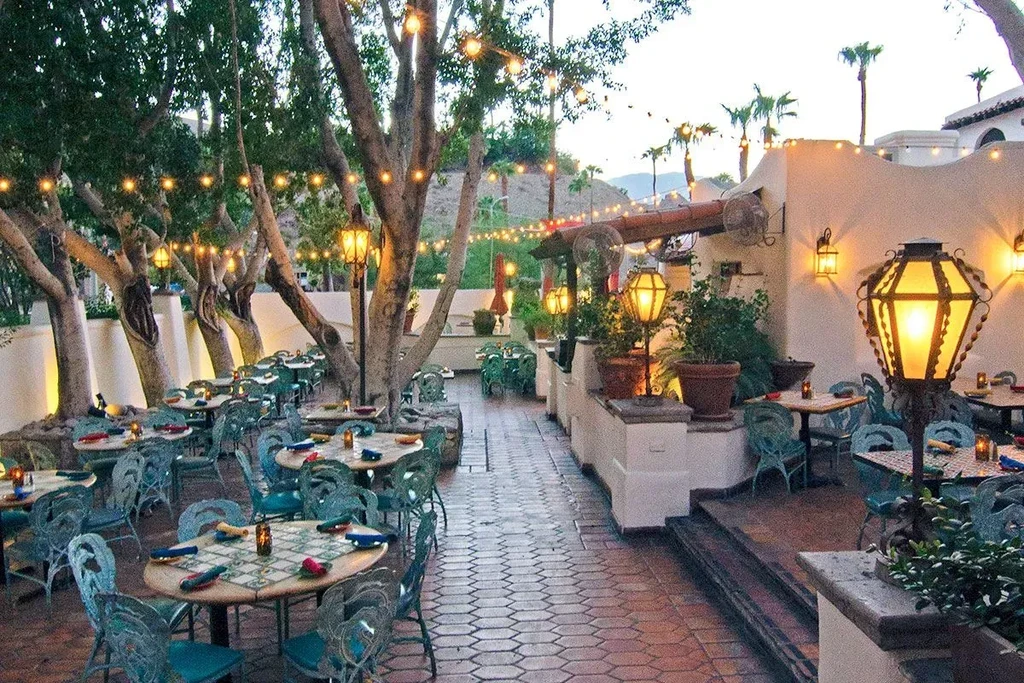 Outdoor restaurant patio with lit trees, lanterns, and empty tables at dusk.