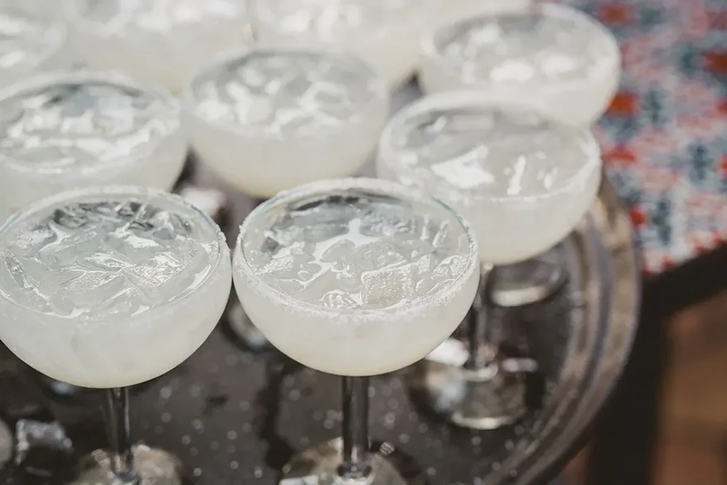 Several glasses of light iced drinks with salted rims on a dark tray.