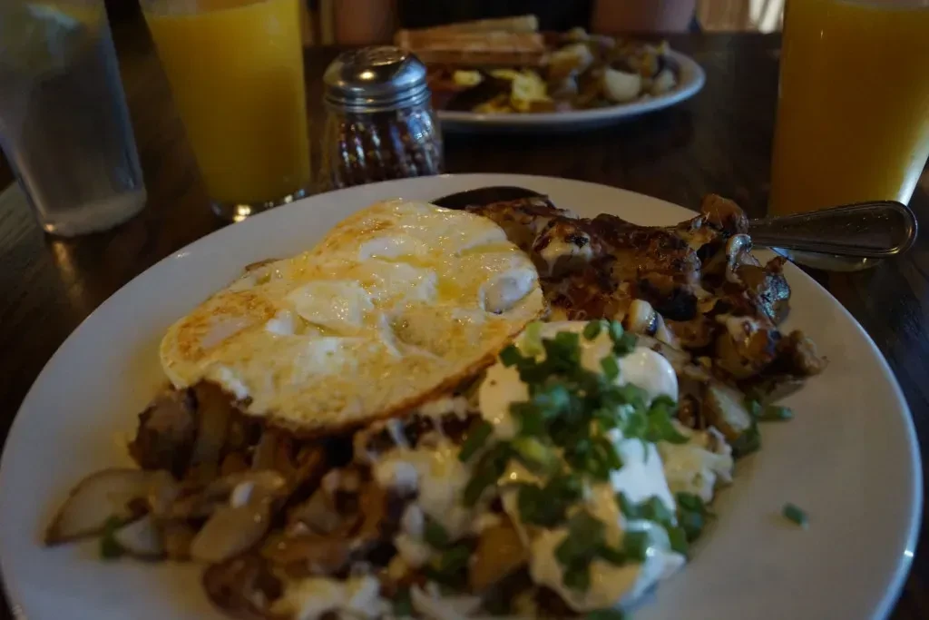 Hearty breakfast plate: fried eggs, roasted potatoes, sauce, green onions.