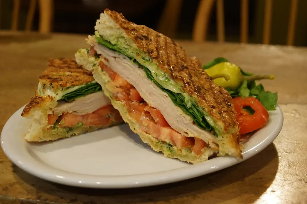 Grilled turkey panini, cut in half, with lettuce, tomato, and pesto.