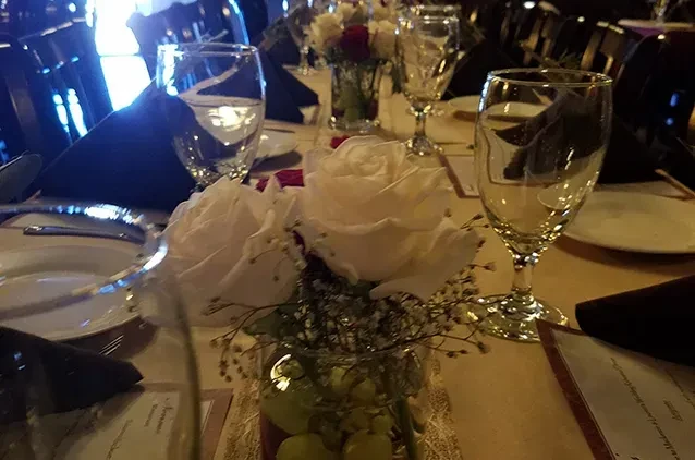 Elegant dining table set with white rose, grape centerpiece, and dark napkins.