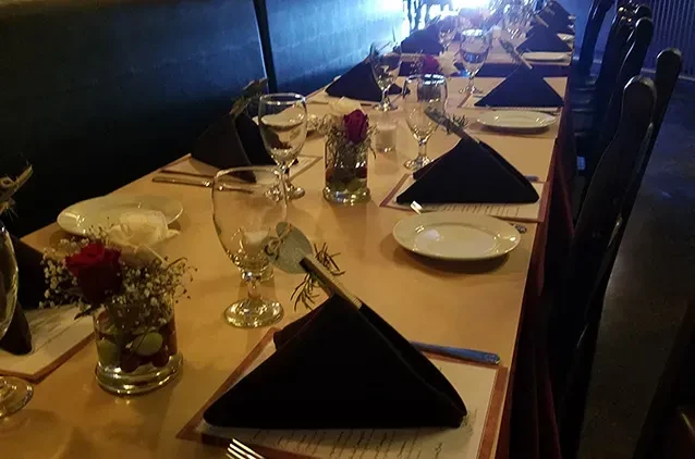 Empty, dimly lit dining table set with rose centerpieces.