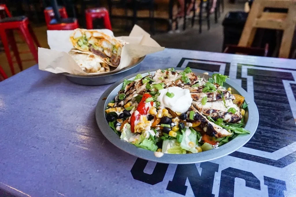 Grilled chicken salad and a cut wrap in metal bowls.
