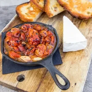Overhead: Skillet of roasted cherry tomatoes, with toast and white cheese.