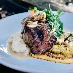 Grilled steak with creamy sauce, mushrooms, mashed potatoes, roasted vegetables.