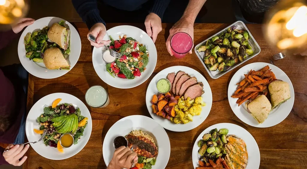 Overhead shot of a table with diverse food, drinks, and diners' hands.