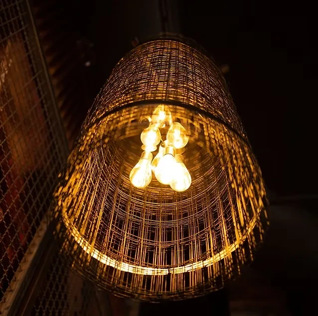 Upward view of a large conical mesh chandelier with amber Edison bulbs.