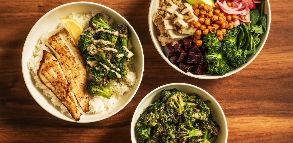 Overhead: three white bowls of healthy meals on a wooden table.