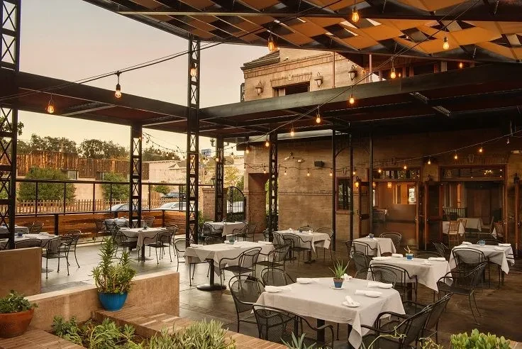 Empty industrial-rustic restaurant patio at dusk with string lights.
