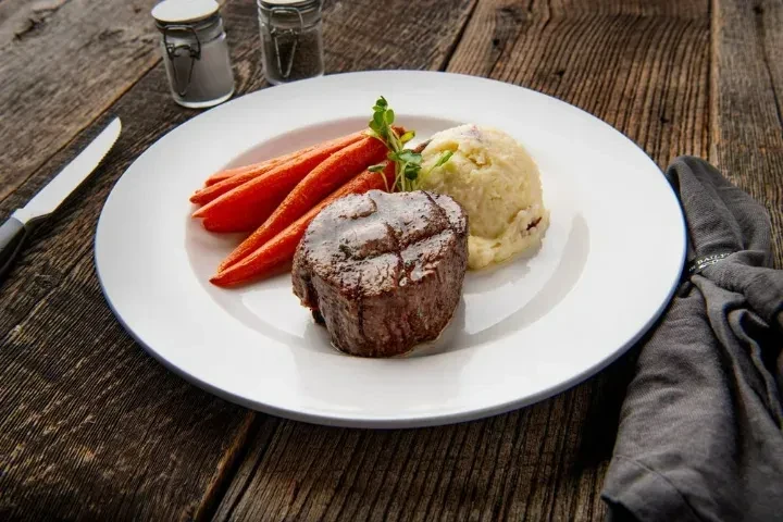 Grilled steak, roasted carrots, and mashed potatoes on a rustic wooden table.