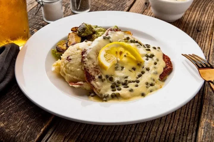 Plated breaded cutlet, creamy sauce, potatoes, Brussels sprouts on rustic table.