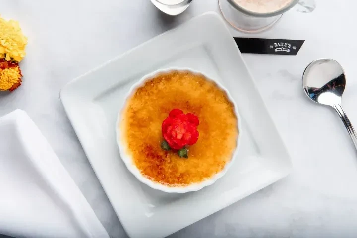 Crème brûlée with caramelized topping, red garnish, yellow flowers, and coffee.