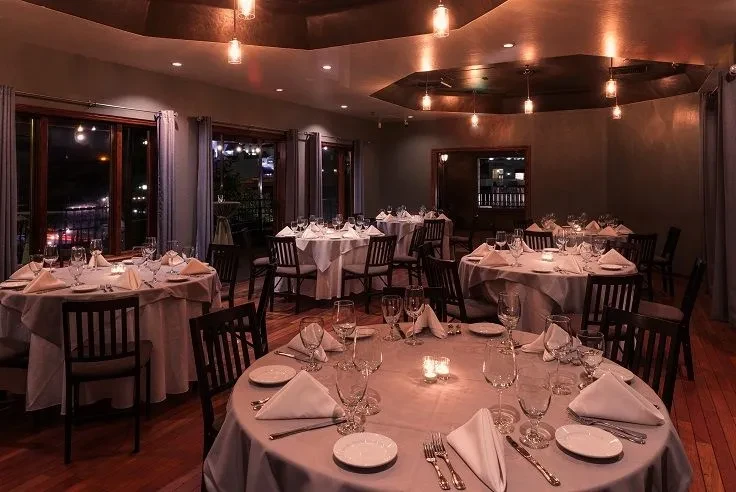 Elegant restaurant dining room at night with set tables and city view.
