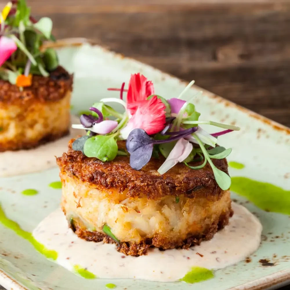 Two golden savory cakes, plated with creamy sauce, microgreens, and edible petals.