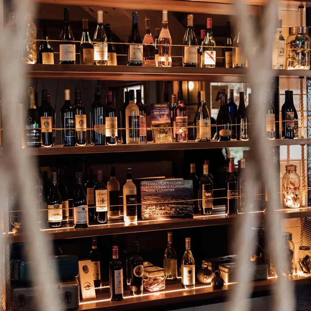 Multi-tiered shelves of wine and spirits, warmly lit, with a wine country book.