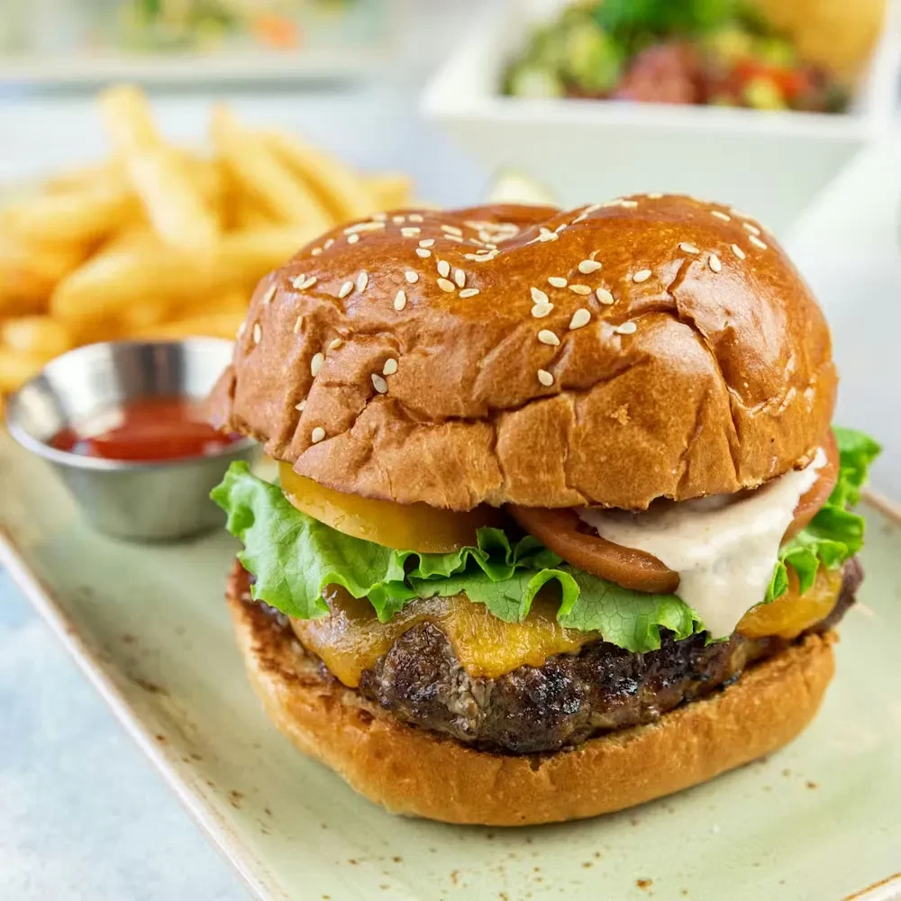 Hamburger with sesame bun, cheese, lettuce, tomato, fries, and ketchup.