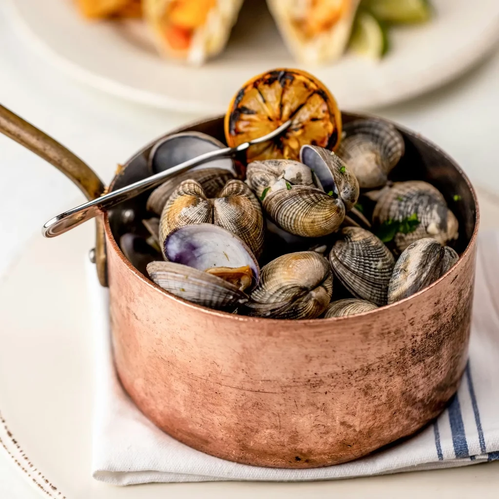 Steamed shellfish in a rustic copper pot with grilled lemon.
