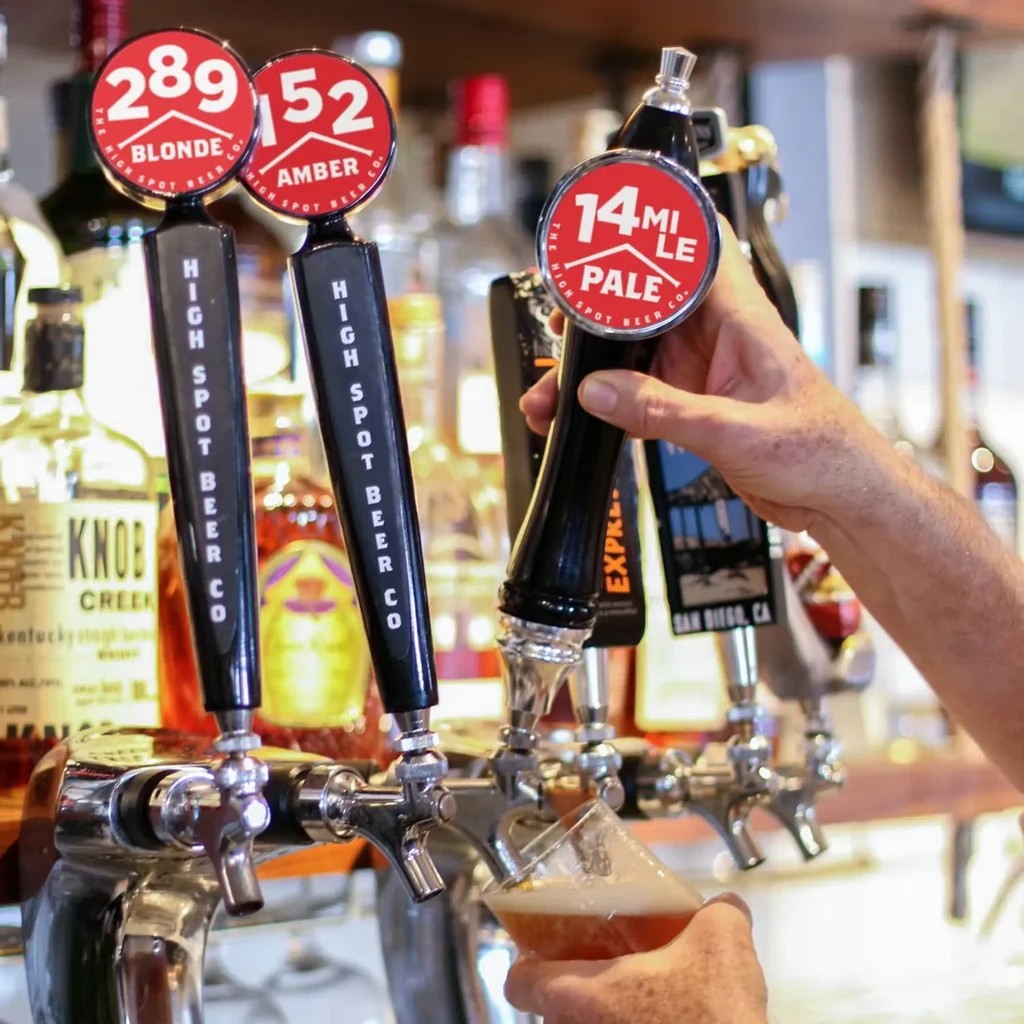 Hand pouring golden beer from a High Spot tap at a bar.