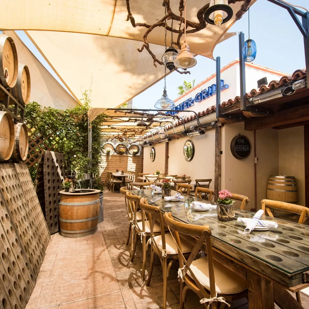 Outdoor dining patio with grapevines, lanterns, wine barrels, and tables.