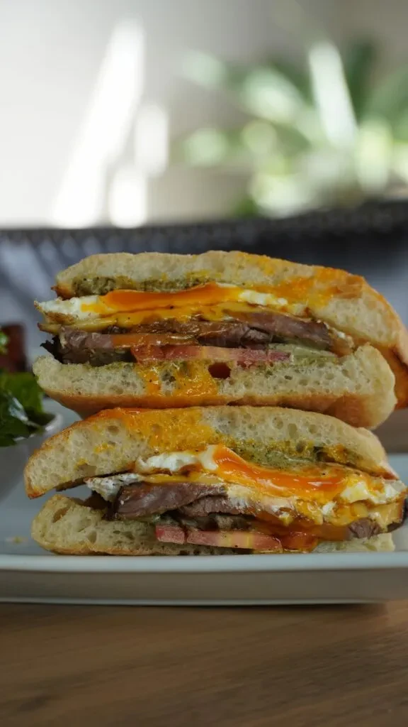 Stacked sandwich with sliced meat, fried egg, tomato, and two sauces.