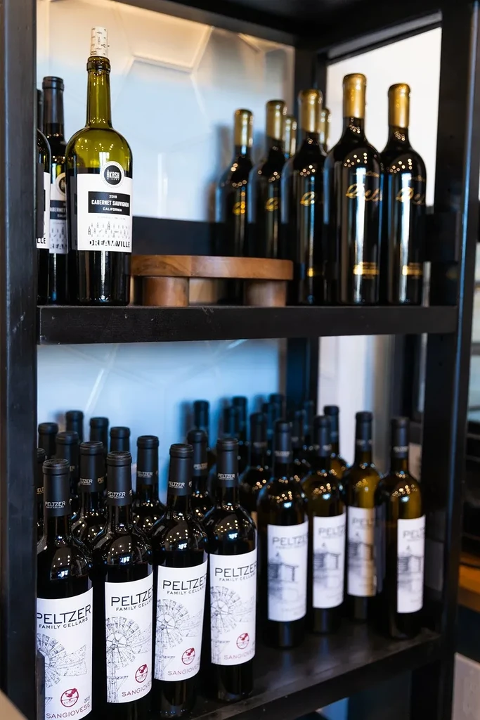 Organized display of Akash and Peltzer wine bottles on dark shelves.
