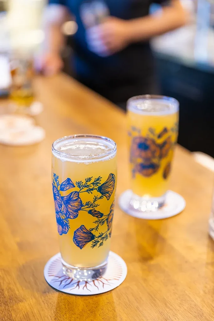 Two floral-designed beer glasses on a wooden bar, one in focus.