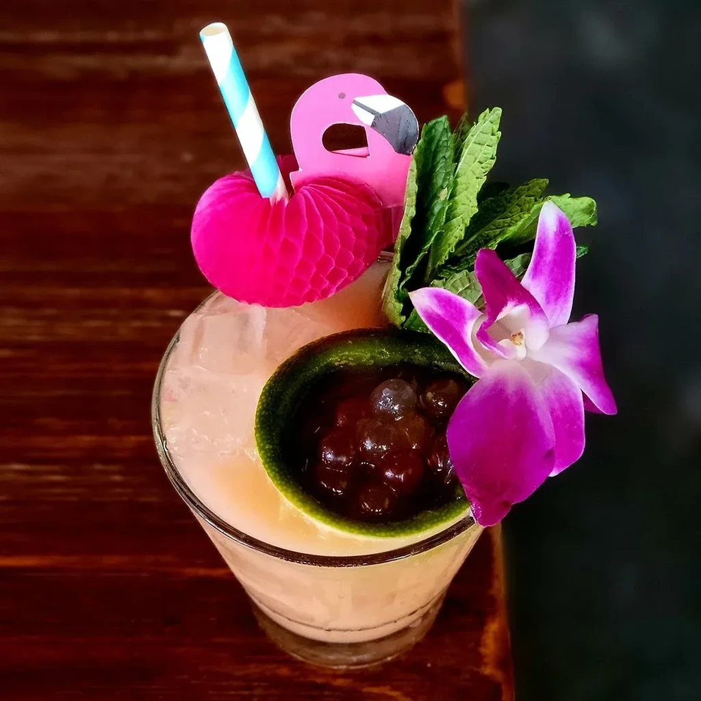Vibrantly garnished tropical cocktail with flamingo, orchid, and boba.